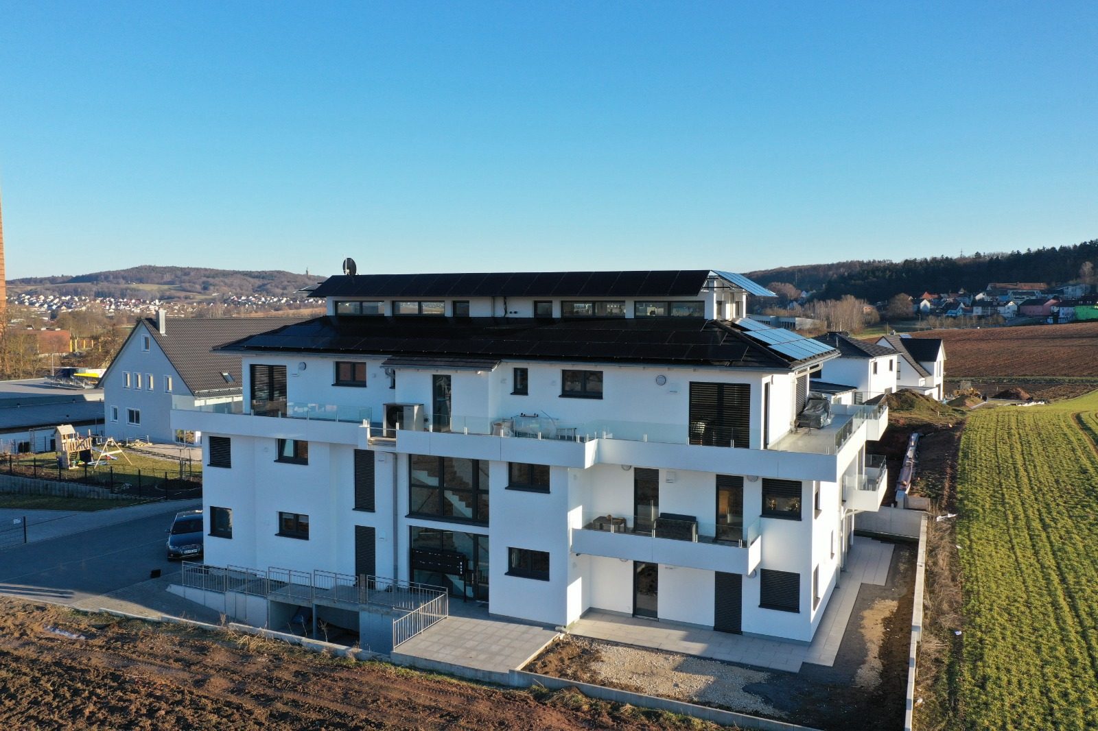 Luftaufnahme eines neu gebauten Mehrfamilienhauses mit vollflächiger schwarzer Photovoltaikanlage auf dem Dach